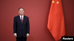 China's Politburo Standing Committee member Wang Qishan, the head of China's anti-corruption watchdog, stands next to a Chinese flag