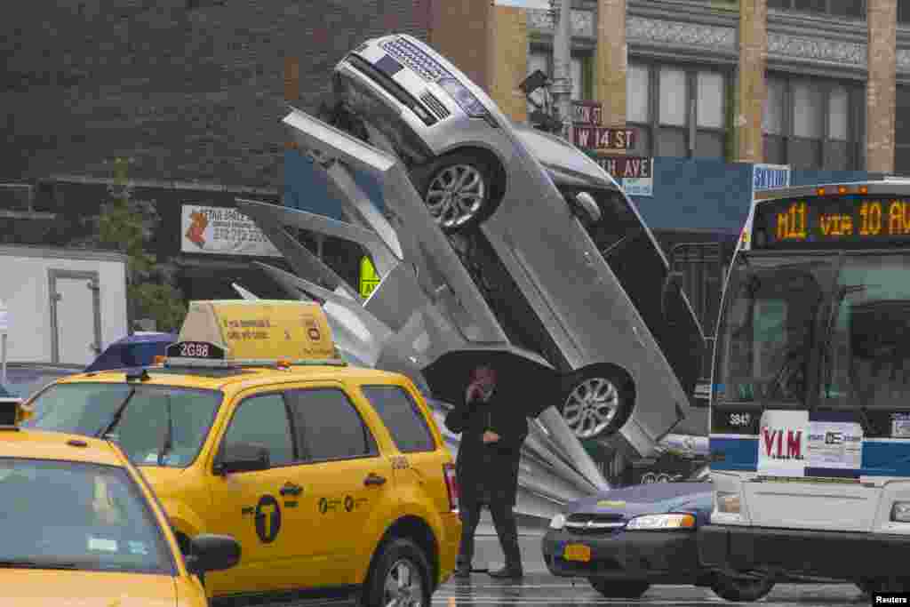 A man with an umbrella walks past an art installation called "Climbing Up" on the streets of Manhattan, New York. The art installation, which was unveiled on June 6, is inspired by the aluminium body of the 2013 Range Rover.