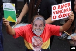 FILE - A demonstrator wearing a mask depicting former Brazilian President Luiz Inacio Lula da Silva, holds a sign with a message that reads in in Portuguese: "Love Will Overcome Hate," and the Brazilian constitution, during a protest in support da Silva,