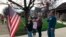 Zach Stamper holds the U.S. flag while his sister Juliette and parents Jennifer and Tim recite the Pledge of Allegiance in the driveway of their home, as next door neighbor, Ann Painter, left, participates in Kettering, Ohio, April 7, 2020.