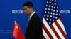 FILE - A Chinese official walks by a China and U.S. national flags ahead of a meeting between Chinese and U.S. negotiators at the Ministry of Commerce in Beijing, Aug. 28, 2023.