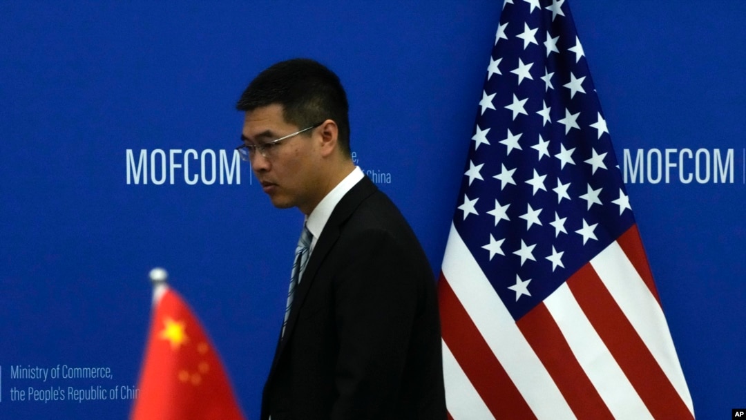 FILE - A Chinese official walks by a China and U.S. national flags ahead of a meeting between Chinese and U.S. negotiators at the Ministry of Commerce in Beijing, Aug. 28, 2023.