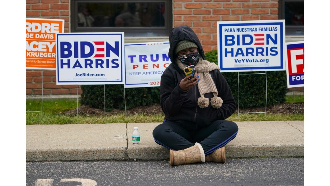 A voter sits on the sidewalk as voters wait in long lines to cast their ballots during early voting at St. Luke's United Methodist Church in Indianapolis, Oct. 28, 2020. The wait to vote was over 4 hours.