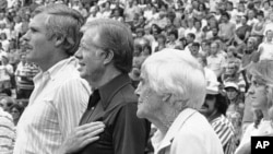 FILE - Atlanta Braves owner Ted Turner, left, sings the National Anthem in Atlanta with former President Jimmy Carter and his mother, Miss Lillian, before the first game of a doubleheader with the Los Angeles Dodgers, July 30, 1982.