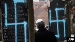 Foto ilustrasi yang menunjukkan seorang pria berjalan di antara kuburan-kuburan yang dicoreti gambar swastika di pemakaman Yahudi di Quatzenheim, 19 Februari 2019. (Foto: AFP)