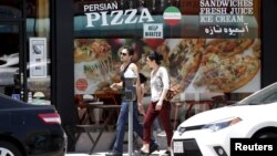 FILE - A couple walks past a Persian pizza restaurant near Persian Square in Westwood, Los Angeles.