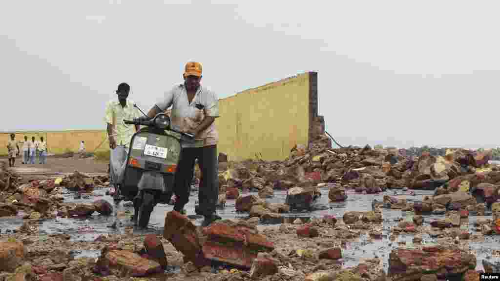 People walk among debris from a broken wall after it was damaged by a wave brought by Cyclone Phailin at a fishing harbor in Visakhapatnam district in Andhra Pradesh.
