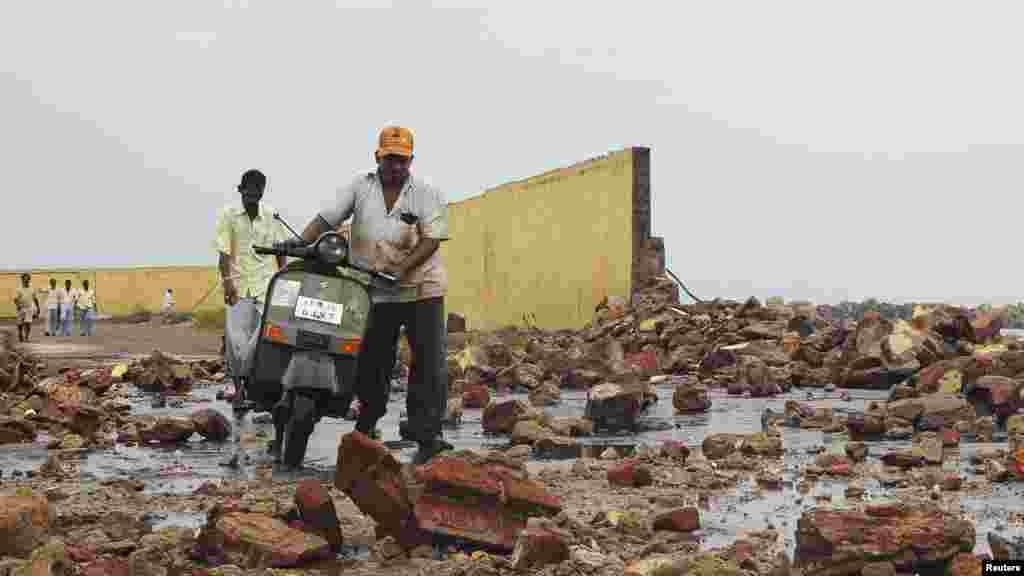 Warga berjalan di antara puing-puing dinding yang dihantam ombak yang dibawa oleh Topan Phailin di pelabuhan nelayan di distrik Visakhapatnam, negara bagian Andhra Pradesh. (Reuters//R Narendra)