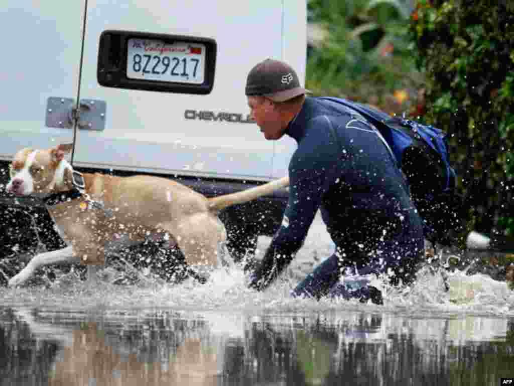 A man and his dog make their way through a flooded street after heavy rain flooded parts of San Diego.