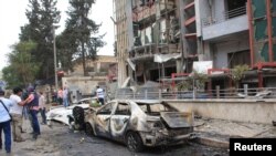 Jurnalis dan warga sipil berdiri dekat kerusakan akibat roket-roket yang dilepaskan pemberontak di Aleppo, Suriah (3/5). 