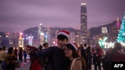 A couple clad in Santa hats pose for a selfie as the city skyline is seen along Hong Kong's Victoria Harbor, Dec. 25, 2018.