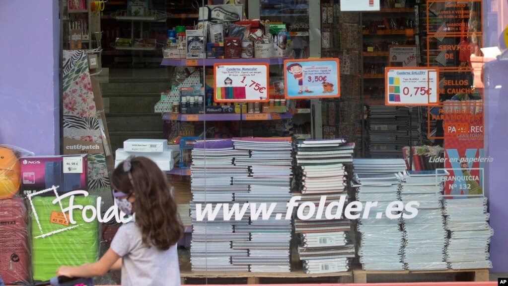 A young girl wearing a face mask walks past a store displaying a coronavirus information poster and selling children's school stationery, backpacks, protective masks and hand sanitizers in Madrid, Spain, Monday, Aug. 24, 2020.