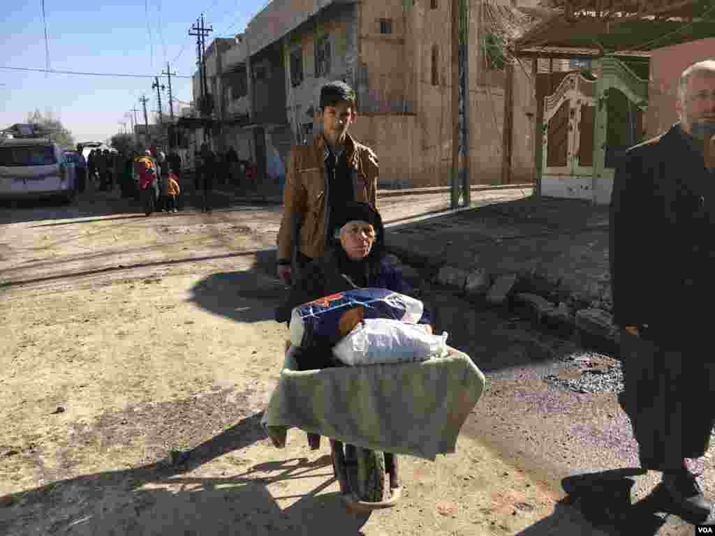 An elderly refugee women is seen being transported in a wheel barrow, in Mosul, Iraq, Jan. 12, 2017. (K. Omar/VOA Kurdish)