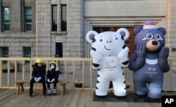 FILE - Children sit next to the 2018 Pyeongchang Winter Olympic Games' official mascots, a white tiger Soohorang, for the Olympics, and black bear Bandabi, right, for the Paralympics, near Seoul Plaza Ice Rink in Seoul, South Korea, Jan. 2, 2018.
