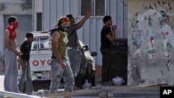 Residents of the Shiite Muslim village of Malkiya, Bahrain, southwest of Manama, watch - some with stones in hand and others photographing riot police and tanks moving in - Sunday, March 20, 2011