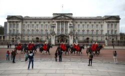 FILE - Royal horse guards ride in front of Buckingham Palace while people look on, in London, Britain, March 20, 2020.