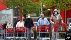 People wearing protective masks queue up to go in a garden store in Munich, Germany, April 20, 2020. 