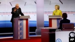 ສະມາຊິກສະພາສູງ Bernie Sanders (ຊ້າຍ) ພວມກ່າວຊີ້ແຈງ ໃນຂະນະທີ່ທ່ານນາງ Hillary Rodham Clinton ຮັບຟັງ ໃນລະຫວ່າງການໂຕ້ວາທີ ຂອງພັກເດໂມແຄຣັດ ທີ່ມະຫາວິທະຍາໄລ ວິສຄັນຊິນ ໃນເມືອງ Milwaukee.