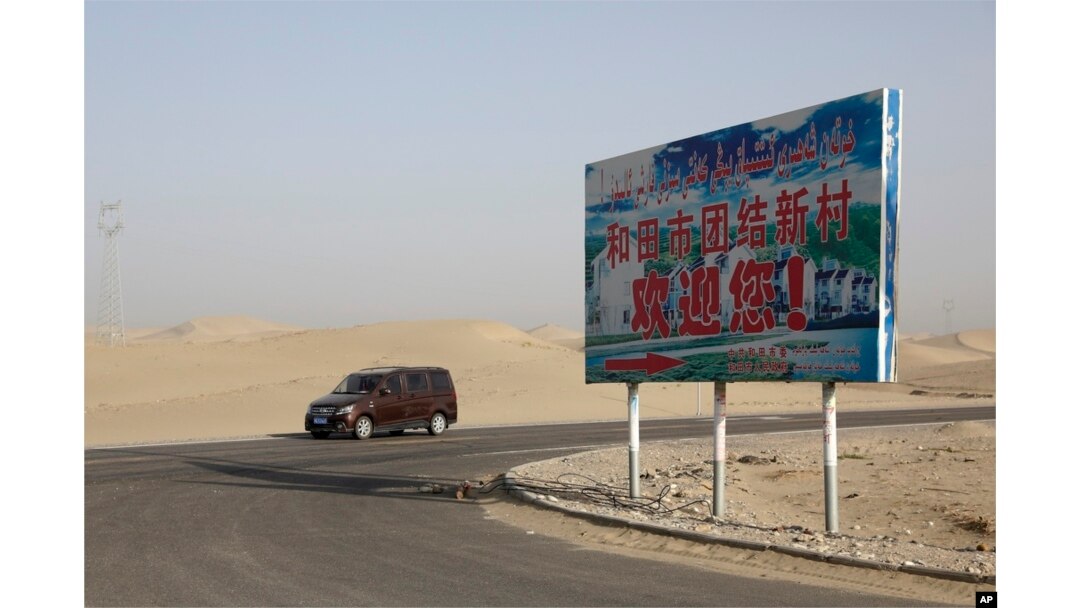 FILE - A car drives by a sign reading "Welcome to the Hotan Unity New Village" in China's Xinjiang region on Sept. 21, 2018. Authorities have been changing the names of villages inhabited by Uyghurs to reflect the ruling Communist Party's ideology.