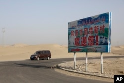 FILE - A car drives by a sign reading 'Welcome to the Hotan Unity New Village' in China's Xinjiang region on Sept. 21, 2018. Authorities have been changing the names of villages inhabited by Uyghurs to reflect the ruling Communist Party's ideology.