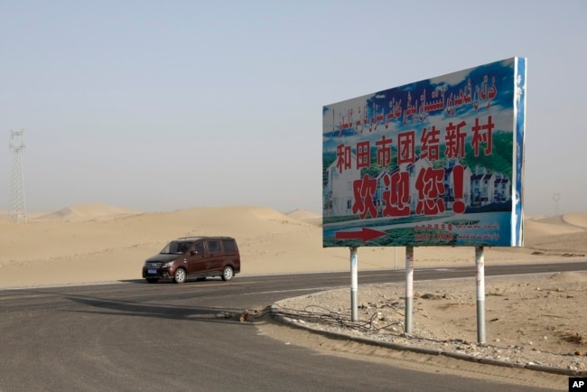 FILE - A car drives by a sign reading "Welcome to the Hotan Unity New Village" in China's Xinjiang region on Sept. 21, 2018. Authorities have been changing the names of villages inhabited by Uyghurs to reflect the ruling Communist Party's ideology.