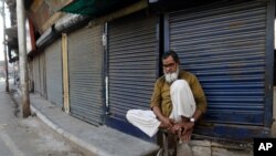 FILE - An Indian Muslim sits in front of closed shops during a coronavirus shutdown in Prayagraj, India, April 5, 2020. 