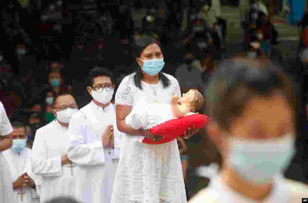 A woman, wearing a face mask, carries a baby Jesus statue, during a procession for a Christmas Mass service at a church in Bali, Indonesia.
