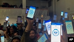 Decenas de migrantes alzan sus teléfonos, el 22 de enero de 2023, mostrando en ellos la app CBPOne, en un albergue en Tijuana, México.
