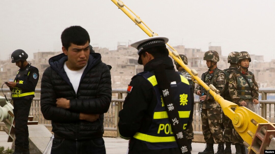 Seorang polisi memeriksa kartu identitas seorang pria sementara pasukan keamanan berjaga di sebuah jalan di Kashgar, Wilayah Otonomi Xinjiang Uighur, China, 24 Maret 2017. 