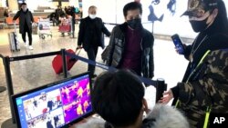 Para petugas bandara mengukur suhu tubuh pendatang dengan thermometer elektronik di Bandara Internasional Tianhe Wuhan di Wuhan, provinsi Hubei, China selatan, Selasa 21 Januari 2020. 