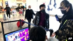 FILE - Travelers pass through a health screening checkpoint at Wuhan Tianhe International Airport in Wuhan in southern China's Hubei province, Jan. 21, 2020.