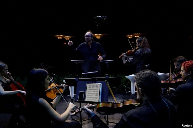 Spanish music director Hache Costa rehearses prior to performing an adaptation of Antonio Vivaldi's famous “The Four Seasons” concertos as a screen shows an image of flowers in spring in Madrid, Spain, October 24, 2023. (REUTERS/Susana Vera)