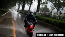 Seorang pria mengendarai skuter listrik Niu melaju melewati genangan air saat badai di Beijing, China, 21 Mei 2020. (Foto: REUTERS/Thomas Peter)