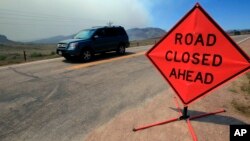 File - Smoke rises in the background as a motorist drives down Larimer County Highway 74W as a wildfire burns, near Livermore, Colorado.