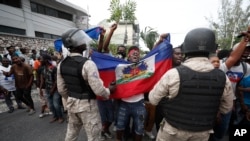 FILE - Anti-government protesters holding a Haitian flag confront security forces during a march in Port-au-Prince, Haiti, Oct. 20, 2019. 