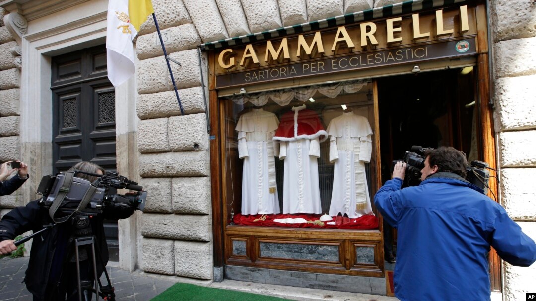 FILE - TV crews film Gammarelli tailoring shop window where three sets of papal outfits - small, medium and large sizes - which will be sent to the Vatican for the new pope, are displayed, in Rome.