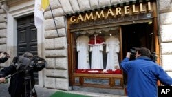 FILE - TV crews film Gammarelli tailoring shop window where three sets of papal outfits - small, medium and large sizes - which will be sent to the Vatican for the new pope, are displayed, in Rome.