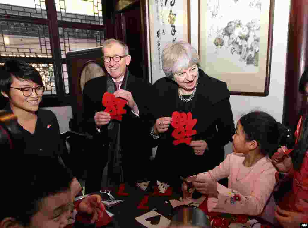 2018年2月2日，英国首相特蕾莎·梅（Theresa May）和她的丈夫菲利普·梅在上海豫园观看学生剪纸，手里拿着福字。