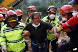 Rescue workers help a woman after she identified two family members as their bodies are retrieved from the site of a mudslide in Cambray, a neighborhood in the suburb of Santa Catarina Pinula, on the outskirts of Guatemala City, Oct. 3, 2015.