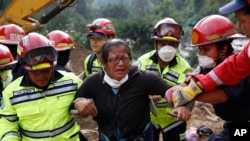 Rescue workers help a woman after she identified two family members as their bodies are retrieved from the site of a mudslide in Cambray, a neighborhood in the suburb of Santa Catarina Pinula, on the outskirts of Guatemala City, Oct. 3, 2015. 