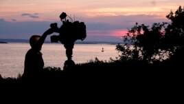 A member of a TV crew adjusts their camera while filming near the shore of Bailey Island, Maine, where a woman swimming off the coast was killed in an apparent shark attack Monday, July 27, 2020. (AP Photo/Jim Gerberich)