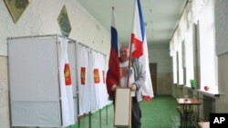 A polling station official with Russian national and Crimea flags is prepared for the 2018 Russian presidential election, in Simferopol, Crimea, March 17, 2018.