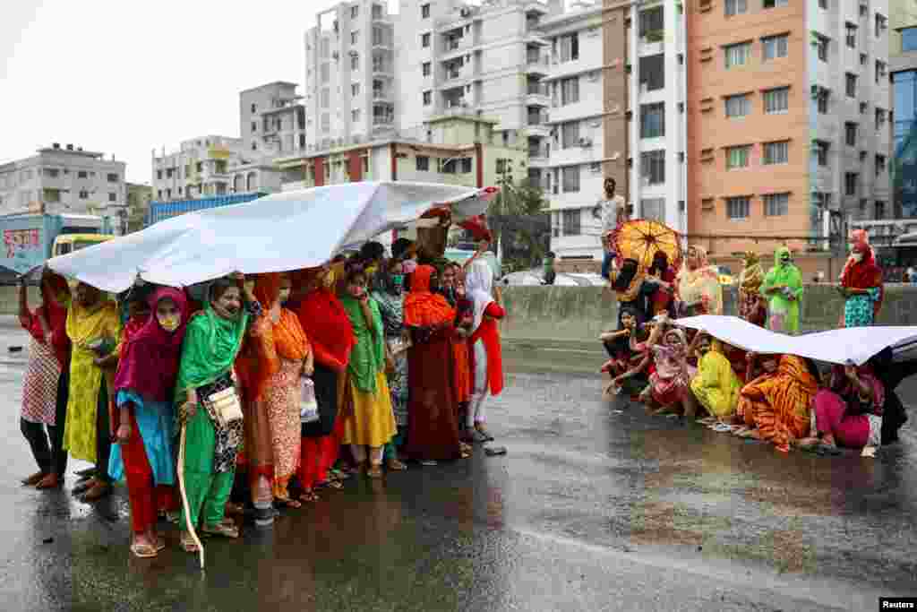 Garments workers take shelter when it starts to rain as they block a road demanding their due wages during the the coronavirus lockdown in Dhaka, Bangladesh.