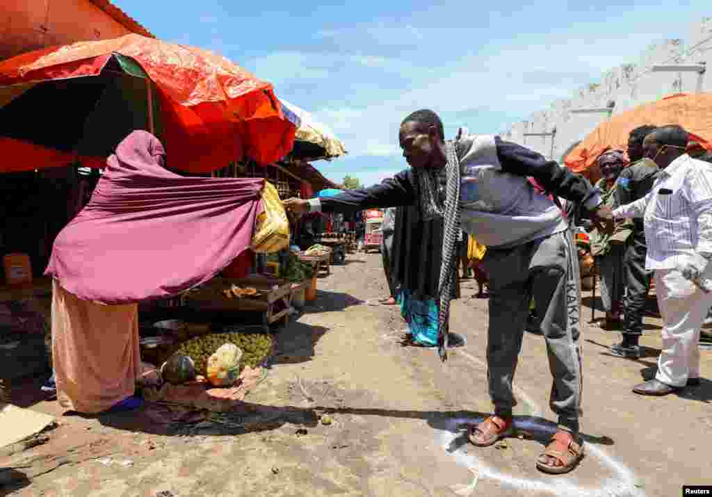 A Somali woman sells fruit to a person standing at a social distancing marking drawn on the ground, at the market center in Hamarweyne district in Mogadishu, Somalia.