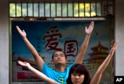 Employees of a Chinese bank take part in a motivation exercise at Ritan Park in Beijing, Sept. 9, 2013. The word of a propaganda poster, background, reads 'Patriotism.'