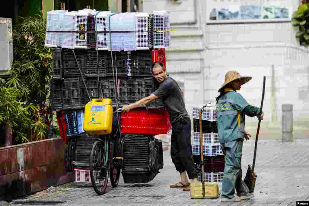 A man moves a bicycle loaded with plastic boxes as he passes a woman cleaning the street in Guangzhou, Guangdong province, China.