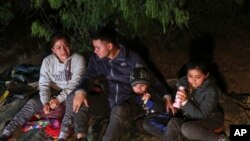 Une famille du Honduras est assise sur le sol après avoir traversé clandestinement le Rio Grande sur un radeau gonflable, à Roma, au Texas, le samedi 27 mars 2021. 