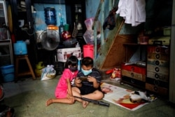 Anak-anak mengenakan masker sambil memainkan ponsel di dalam sebuah rumah di kawasan padat penduduk di Jakarta saat pandemi virus corona (Covid-19), 1 April 2020. (Foto: Reuters)