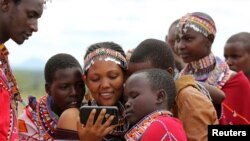 FILE - Maasai girls and a man watch a video on a mobile phone prior to the start of a social event advocating against harmful practices such as female genital mutilation at the Imbirikani Girls High School in Imbirikani, Kenya, April 21, 2016.