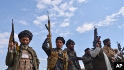 FILE - Afghan militia men raise their weapons as they stand guard in the Achin district of Nangarhar province east of Kabul, Afghanistan.